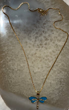 Load image into Gallery viewer, Gold necklace with a blue dragonfly pendant on a textured surface