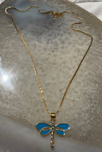 Load image into Gallery viewer, Gold necklace with a blue dragonfly pendant on a reflective surface