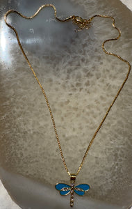 Gold necklace with a blue dragonfly pendant on a textured surface