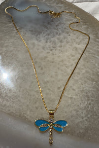 Gold necklace with a blue dragonfly pendant on a reflective surface